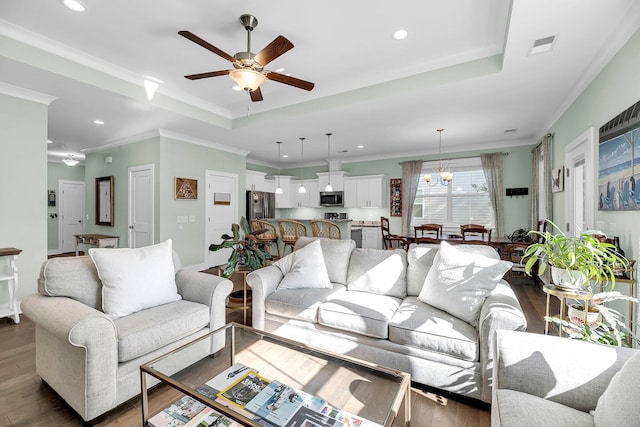 living room with a raised ceiling, ceiling fan with notable chandelier, dark hardwood / wood-style floors, and ornamental molding