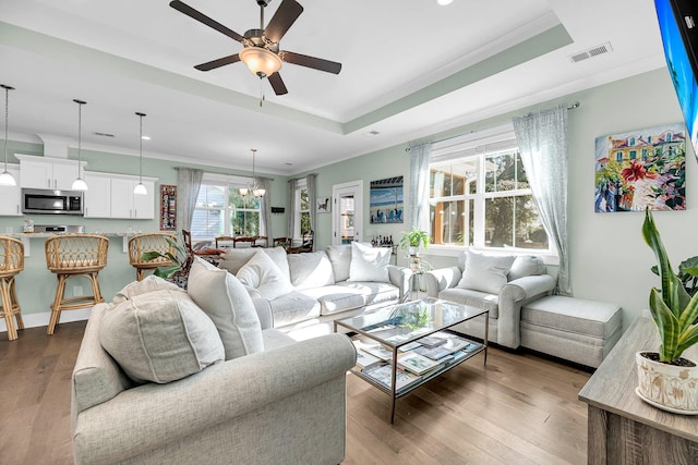 living room with a tray ceiling, ceiling fan with notable chandelier, dark hardwood / wood-style floors, and ornamental molding