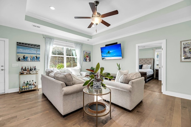 living room featuring wood-type flooring, a tray ceiling, ceiling fan, and crown molding