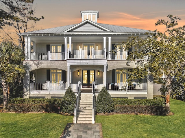 view of front of property with french doors, a balcony, a porch, and a lawn