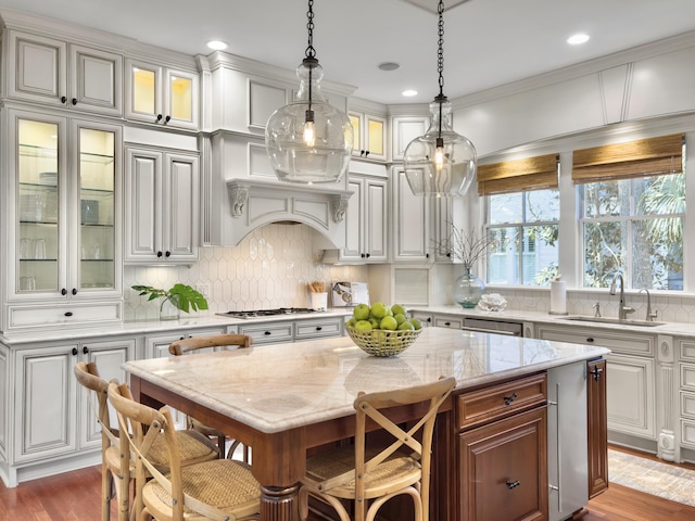 kitchen featuring sink, hanging light fixtures, a kitchen island, light stone counters, and stainless steel gas cooktop