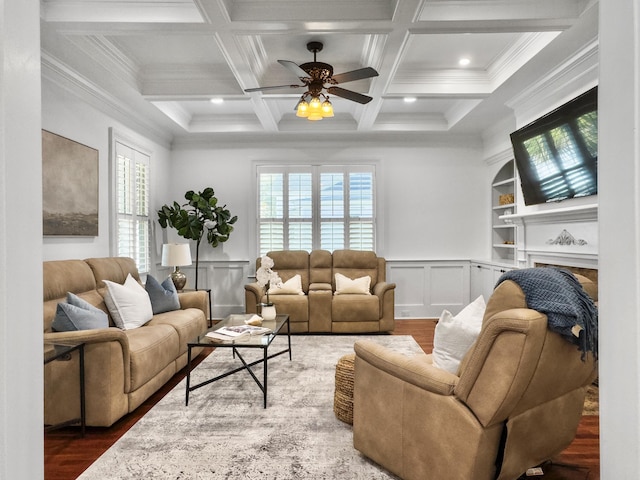 living room with beam ceiling, built in shelves, ceiling fan, coffered ceiling, and ornamental molding