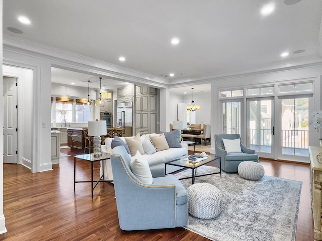 living room featuring a chandelier, ornamental molding, dark wood-type flooring, and a healthy amount of sunlight