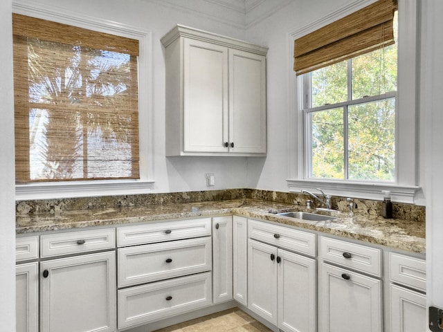 kitchen with white cabinets, light stone counters, and sink