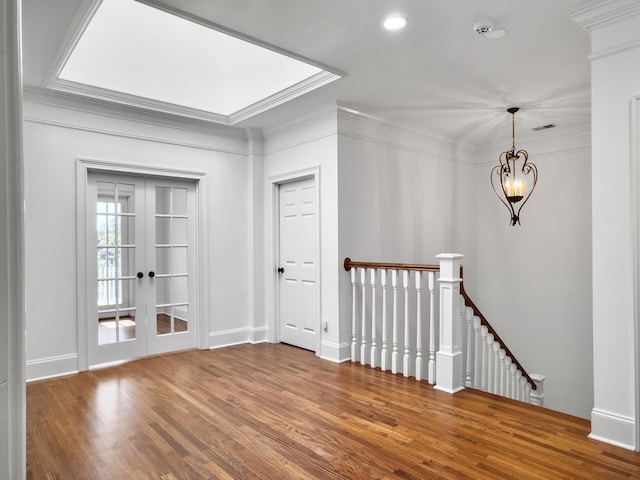 unfurnished room with hardwood / wood-style flooring, a notable chandelier, crown molding, and french doors