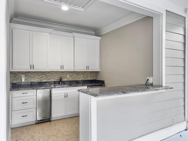 kitchen with backsplash, crown molding, dark stone countertops, white cabinetry, and kitchen peninsula