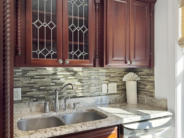 kitchen featuring light stone countertops, backsplash, stainless steel dishwasher, and sink