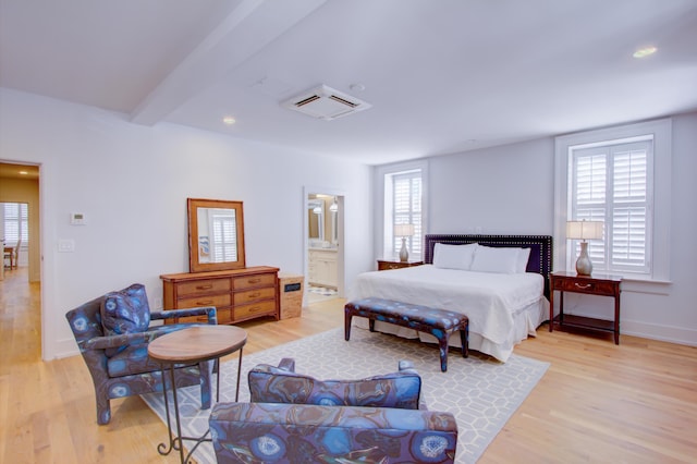 bedroom featuring beam ceiling, connected bathroom, multiple windows, and light wood-type flooring