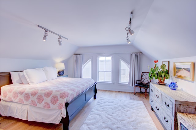 bedroom featuring lofted ceiling, rail lighting, and light hardwood / wood-style flooring