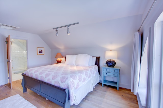 bedroom featuring vaulted ceiling, light wood-type flooring, and ensuite bath