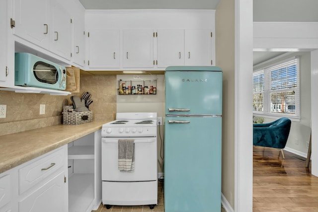 kitchen with white electric range oven, decorative backsplash, light wood-style floors, freestanding refrigerator, and white cabinets