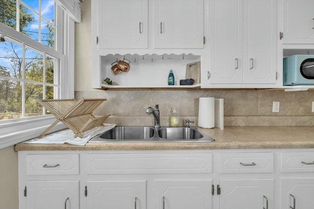 kitchen with a sink, white cabinets, light countertops, backsplash, and open shelves