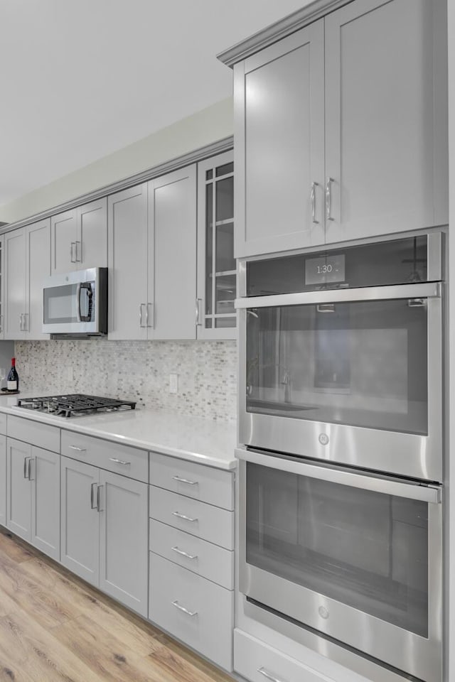 kitchen with decorative backsplash, stainless steel appliances, light hardwood / wood-style floors, and gray cabinetry