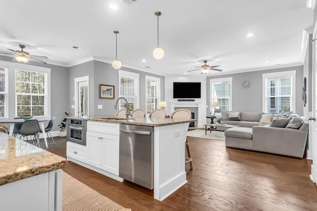 kitchen with hanging light fixtures, appliances with stainless steel finishes, an island with sink, light stone countertops, and white cabinets