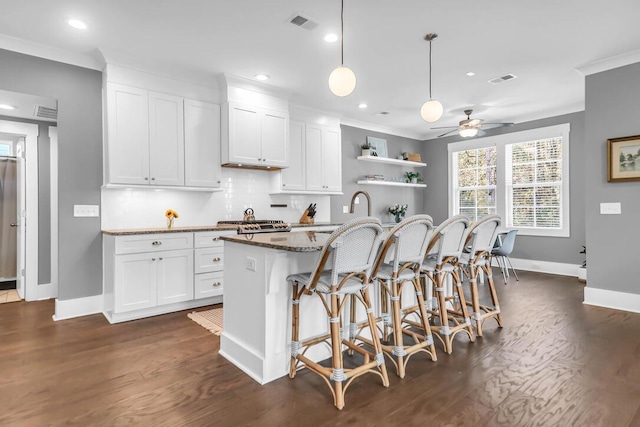 kitchen with dark stone countertops, a center island with sink, white cabinets, a kitchen bar, and decorative light fixtures