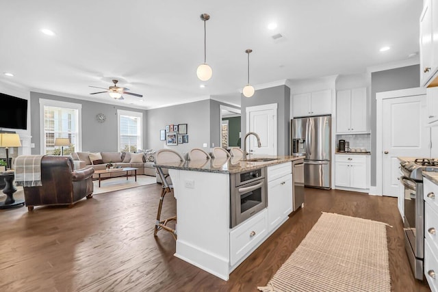 kitchen with sink, appliances with stainless steel finishes, a kitchen island with sink, light stone countertops, and white cabinets