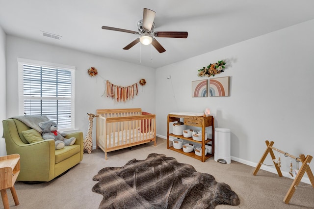 bedroom with carpet floors, visible vents, a ceiling fan, a crib, and baseboards