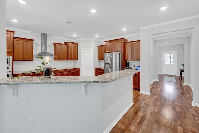 kitchen featuring wood finished floors, visible vents, a kitchen breakfast bar, appliances with stainless steel finishes, and wall chimney exhaust hood