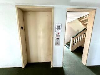 corridor featuring dark colored carpet and elevator