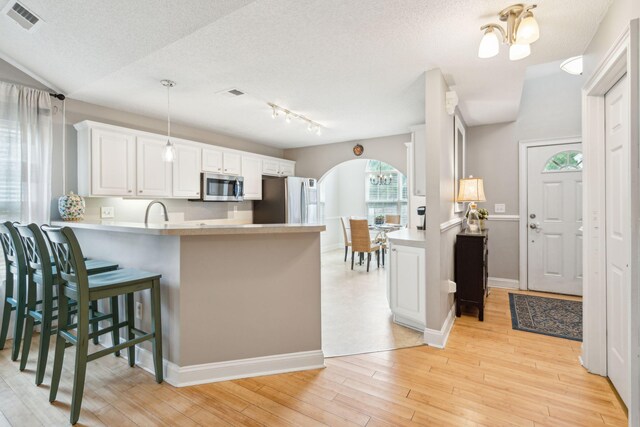 kitchen featuring white cabinets, kitchen peninsula, light hardwood / wood-style flooring, appliances with stainless steel finishes, and an inviting chandelier