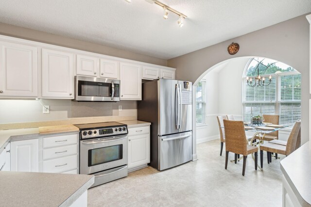 kitchen with white cabinetry, pendant lighting, stainless steel appliances, a textured ceiling, and a notable chandelier