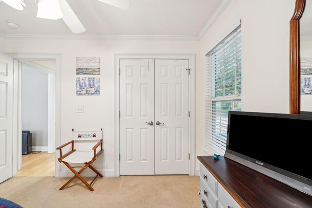 sitting room with ceiling fan, a textured ceiling, crown molding, and light carpet