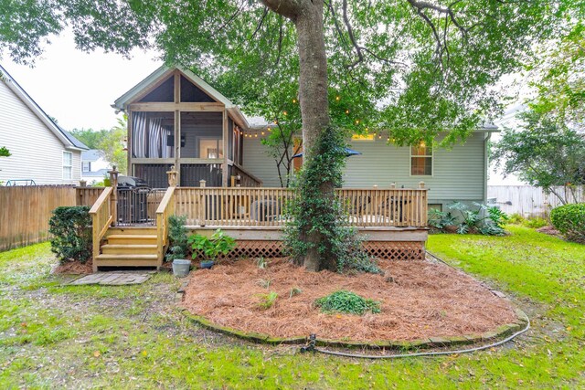 rear view of property with a deck, a sunroom, and a lawn