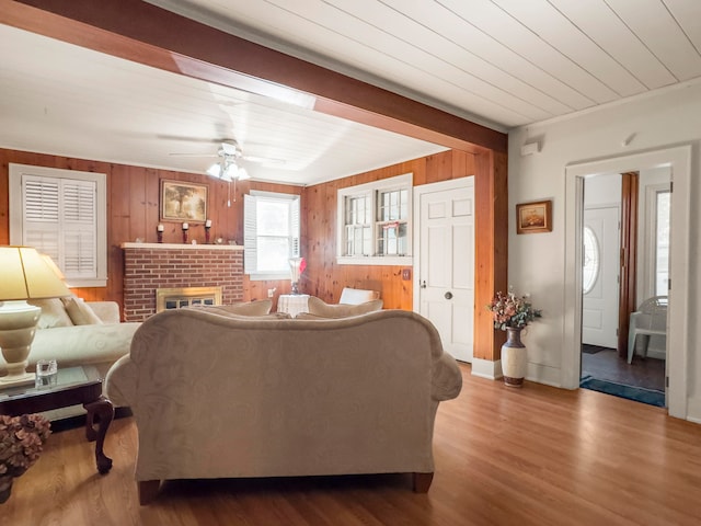 living room featuring a brick fireplace, wood-type flooring, wooden walls, and ceiling fan