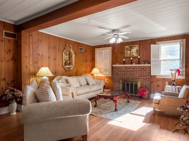 living room with wooden walls, wood-type flooring, ceiling fan, and a brick fireplace