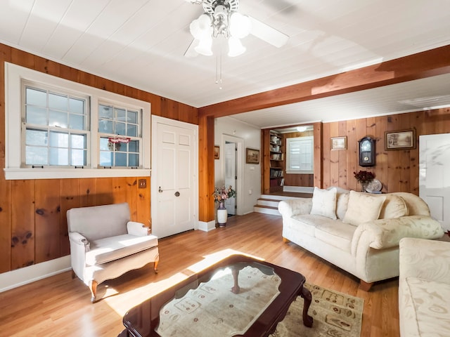 living room with ceiling fan, wooden walls, and light wood-type flooring