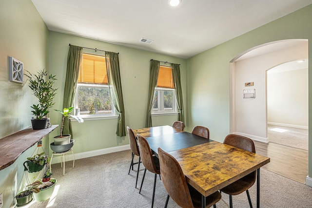 carpeted dining area featuring arched walkways, visible vents, and baseboards