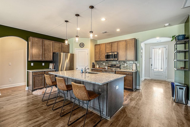 kitchen with arched walkways, appliances with stainless steel finishes, a kitchen breakfast bar, dark wood-type flooring, and backsplash