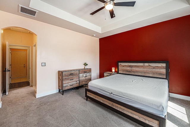 carpeted bedroom featuring arched walkways, baseboards, visible vents, and a tray ceiling