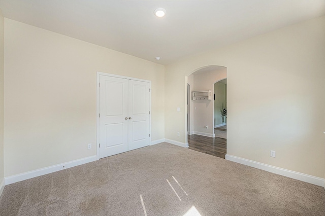 unfurnished bedroom featuring arched walkways, baseboards, carpet, a closet, and a wall mounted AC