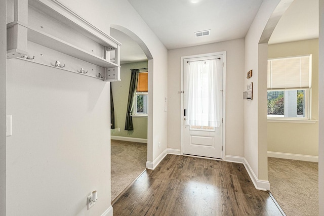 foyer featuring arched walkways, dark wood finished floors, visible vents, and baseboards