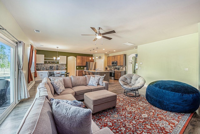 living room with visible vents, arched walkways, wood finished floors, and ceiling fan with notable chandelier