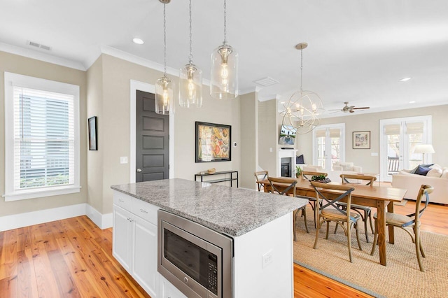 kitchen with white cabinetry, a center island, light wood-style flooring, stainless steel microwave, and visible vents
