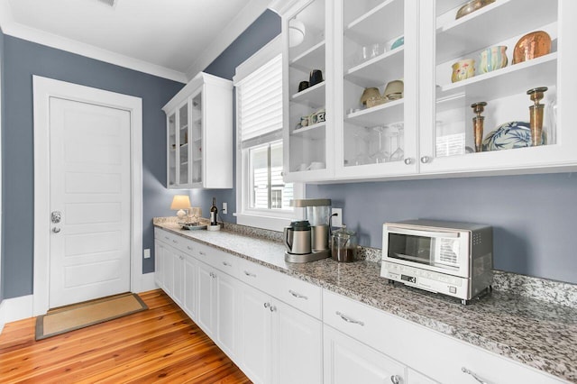 kitchen featuring white cabinetry, ornamental molding, glass insert cabinets, and light wood-type flooring