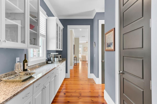 interior space featuring crown molding, white cabinetry, glass insert cabinets, light wood-type flooring, and baseboards
