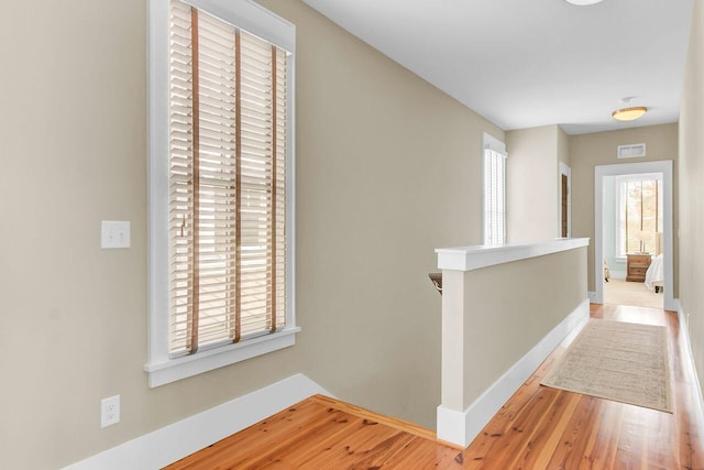 hallway featuring visible vents, an upstairs landing, baseboards, and wood finished floors