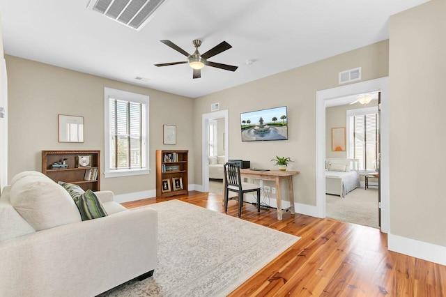 living area featuring baseboards, visible vents, light wood-style floors, and a ceiling fan