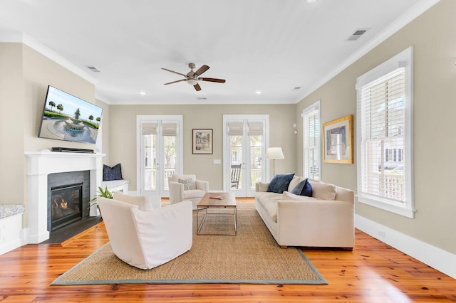 living room featuring a ceiling fan, crown molding, light wood-style floors, and visible vents