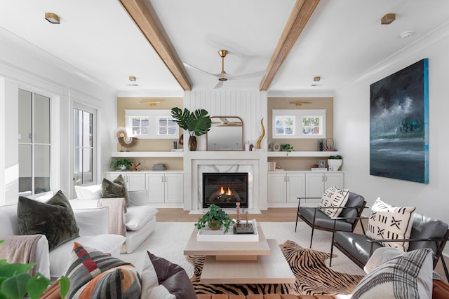 living room with beamed ceiling, crown molding, light wood-type flooring, and a fireplace