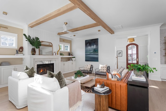 living room featuring beamed ceiling, a healthy amount of sunlight, a premium fireplace, and light hardwood / wood-style flooring