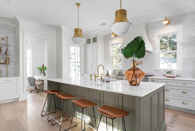 kitchen featuring a kitchen breakfast bar, crown molding, a center island with sink, and light stone counters