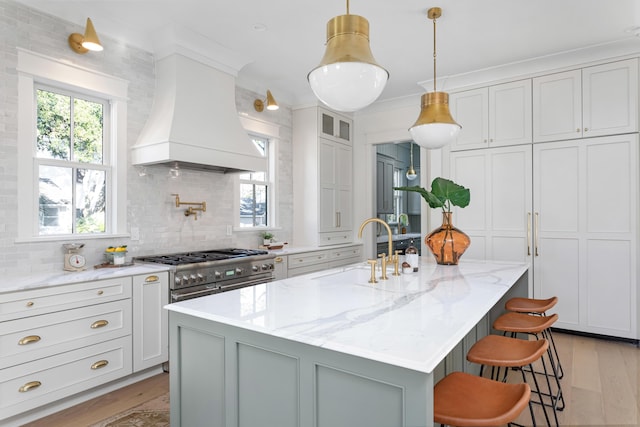 kitchen featuring sink, a breakfast bar, premium range hood, a kitchen island with sink, and light stone counters