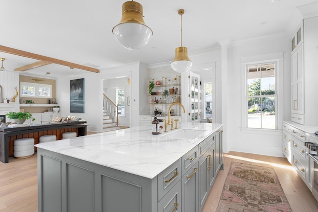 kitchen featuring sink, gray cabinetry, light hardwood / wood-style flooring, pendant lighting, and light stone countertops