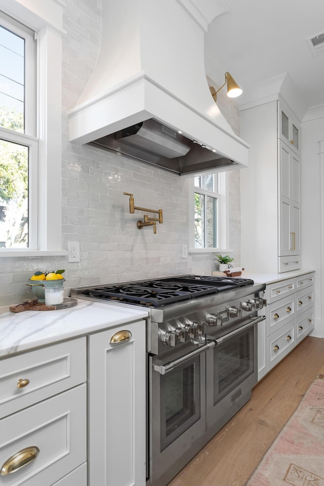 kitchen featuring custom exhaust hood, light stone counters, double oven range, light hardwood / wood-style floors, and white cabinets