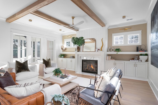 living room with crown molding, ceiling fan, beam ceiling, a fireplace, and light hardwood / wood-style floors