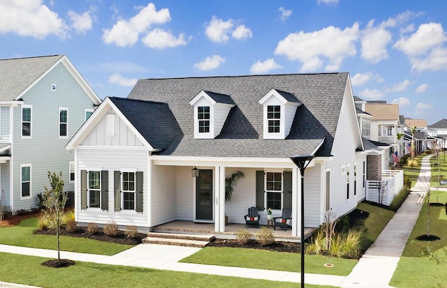 view of front of home with board and batten siding, covered porch, a shingled roof, and a front lawn